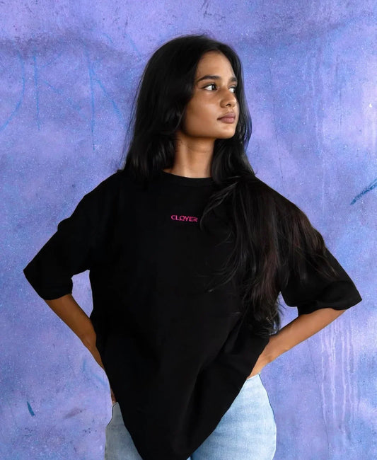 Young woman in black Clover t-shirt and light blue jeans posing against textured purple wall