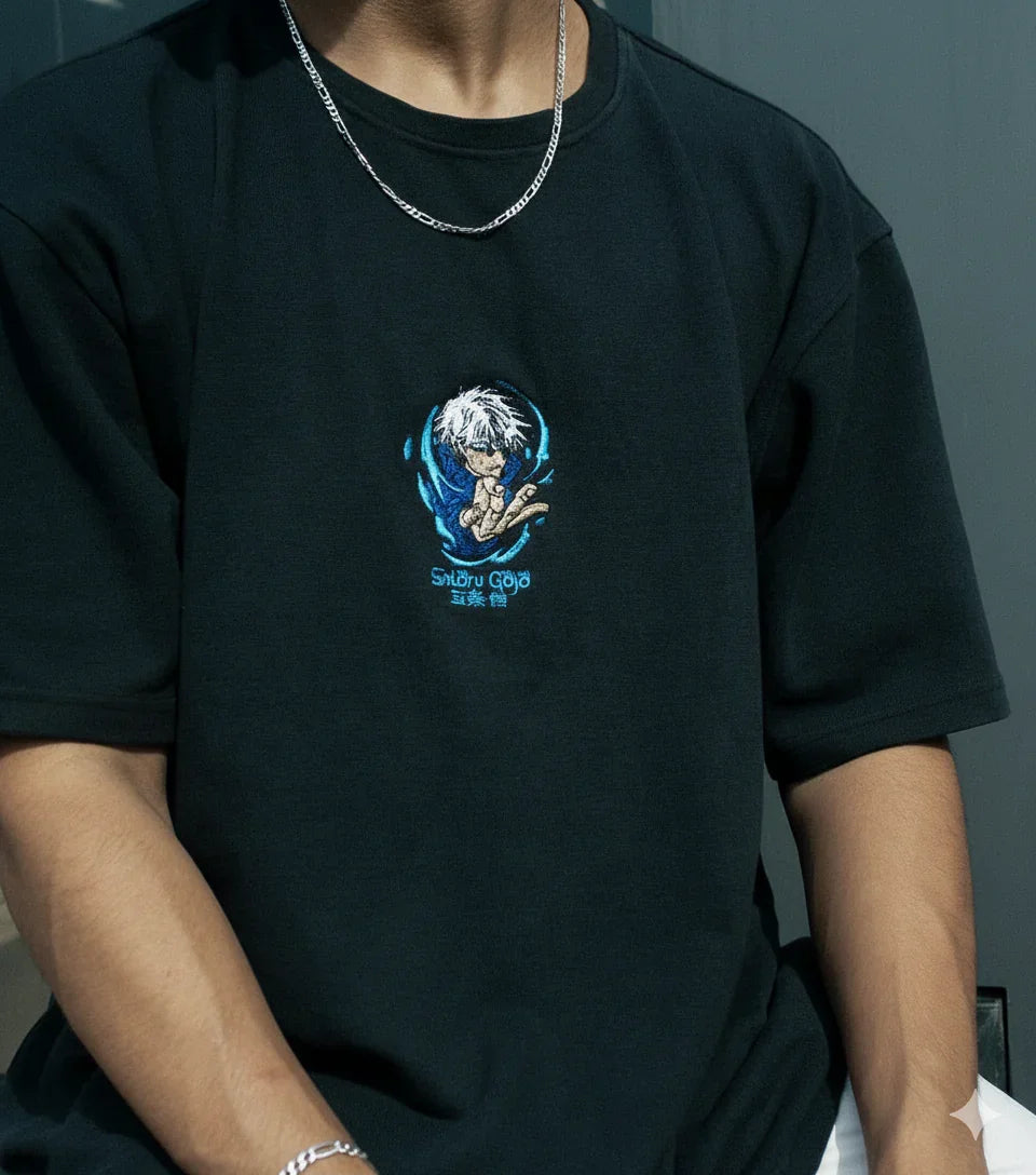 Black t-shirt featuring a small embroidered anime character with white hair and blue accents, worn with silver chain